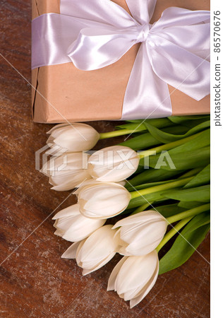 White tulips and gift box tied with white ribbonon the wooden background White tulips and gift box tied with white ribbonon the wooden background 86570676
