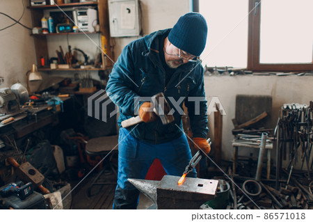 Blacksmith forges and makes metal detail with hammer and anvil at smith farrier forge. 86571018