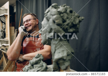 Man sculptor creates sculpt bust clay human woman sculpture and calling client cell mobile phone 86571183