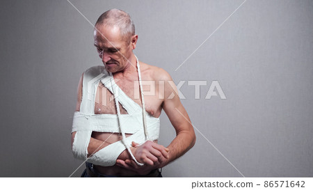 Senior man with bandage examines broken shoulder at wall Senior man with bandage examines broken shoulder at wall 86571642