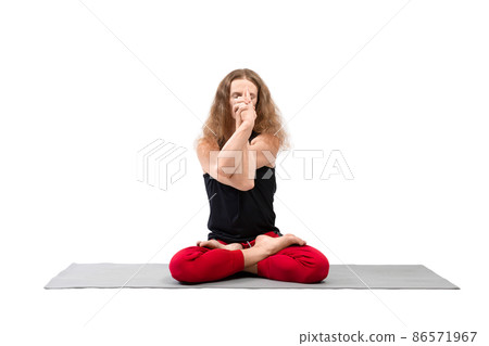 Male yoga. Long-haired blond man with closed eyes sitting in lotus position on a mat with intertwined hands in front of his face, Padmasana, isolated on white. Male yoga. Long-haired blond man with closed eyes sitting in lotus position on a mat with intertwined hands in front of his face, Padmasana, isolated on white. 86571967