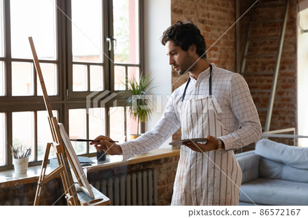 Thoughtful inspired young artist guy drawing at easel Thoughtful inspired young artist guy drawing at easel 86572167