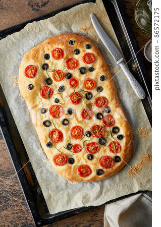 Focaccia, pizza, italian flat bread with tomatoes, olives and rosemary on tray Focaccia, pizza, italian flat bread with tomatoes, olives and rosemary on tray 86572175