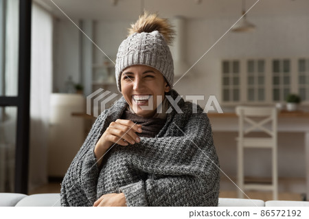 Laughing woman wear hat wrapped in knitted plaid sit indoor Laughing woman wear hat wrapped in knitted plaid sit indoor 86572192