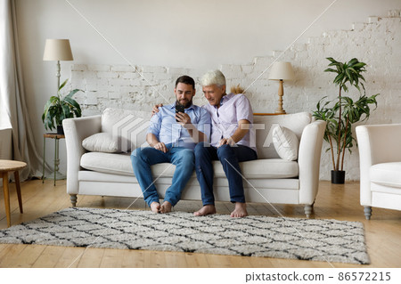 Happy mature grey haired father and grown son sharing smartphone Happy mature grey haired father and grown son sharing smartphone 86572215