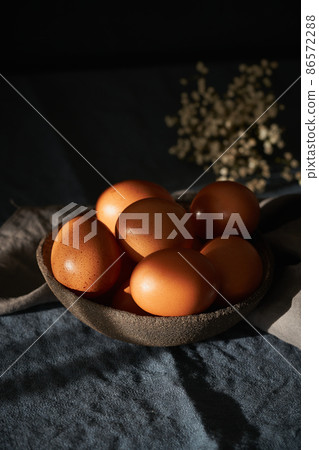 Unusual Easter on dark background. Bowl of brown eggs on dark blue table, flowers. Unusual Easter on dark background. Bowl of brown eggs on dark blue table, flowers. 86572288