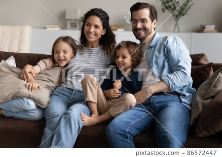 Family sitting on sofa at home smiling looking into distance 86572447