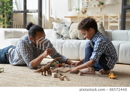 Happy caring young African American father playing toys with son. 86572448