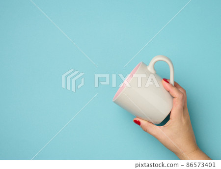female hand holds a ceramic mug on a blue background, break time and drink coffee 86573401