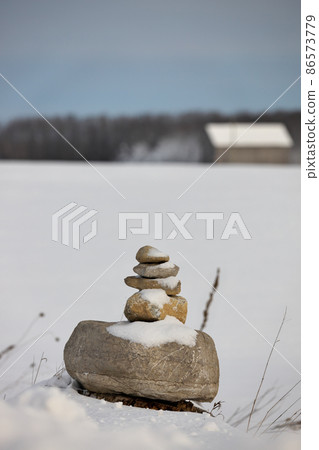 An Inukshuk in a field in the winter with a barn in the distant background An Inukshuk in a field in the winter with a barn in the distant background 86573779