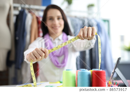 Woman seamstress holds centimeter for taking measurements in atelier Woman seamstress holds centimeter for taking measurements in atelier 86573917