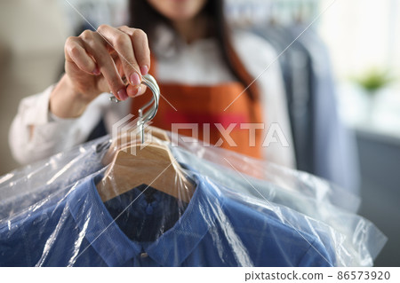 Female receptionist holds out clean suit after being dry cleaned closeup Female receptionist holds out clean suit after being dry cleaned closeup 86573920