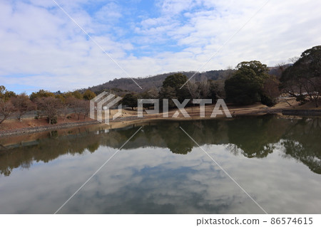 藍天白雲，山巒疊嶂，各種樹木林立，枯草山丘，水鏡面上有池塘，水邊有鹿。 86574615