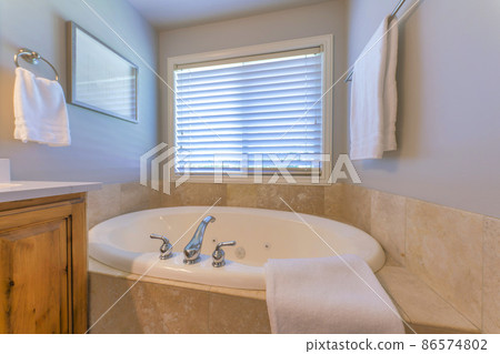 Alcove bathtub with tiles surround near the window with blinds Alcove bathtub with tiles surround near the window with blinds 86574802