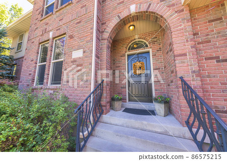 Facade of a house with arched entrance and black front door with yellow wreath and transom window Facade of a house with arched entrance and black front door with yellow wreath and transom window 86575215