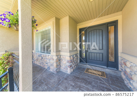 Porch of a house with stone tiles flooring and black front door with two side panels Porch of a house with stone tiles flooring and black front door with two side panels 86575217