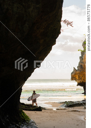 A man walking on the beach with a surfboard. 86575776