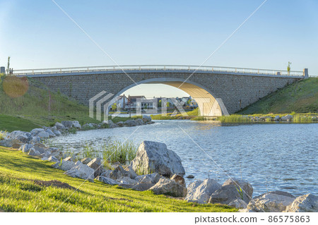 Arched bridge over the Oquirrh Lake with rocks on the shore at Daybreak, Utah 86575863