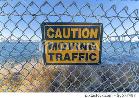 Caution moving traffic sign on a mesh wire fence at Coronado, San Diego, California 86577497