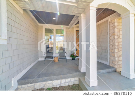 Entrance of a house with porch arched columns and beige shingles siding 86578110