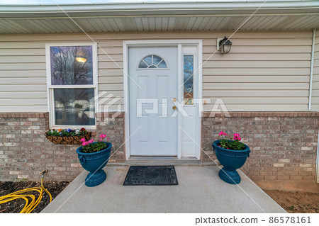 Entrance of a house with white front door with sidelight and two potted flowers at the doorstep Entrance of a house with white front door with sidelight and two potted flowers at the doorstep 86578161