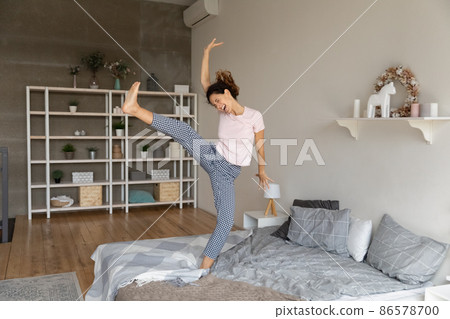 Carefree funny young Hispanic happy woman dancing on the bed 86578700