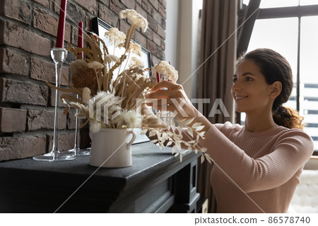 Young Latin female homeowner improving dwelling view with dried flowers 86578740