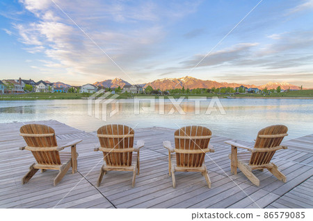 Four wooden lounge chairs facing the reflective Oquirrh Lake at Daybreak, Utah 86579085