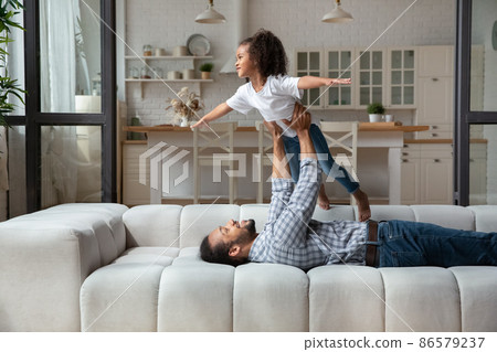 Smiling young African American father lifting daughter in air. Smiling young African American father lifting daughter in air. 86579237