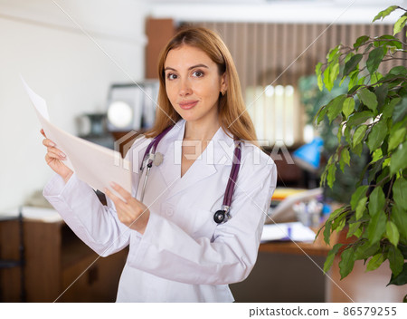 Doctor woman standing in hall with sheets of paper in hands Doctor woman standing in hall with sheets of paper in hands 86579255