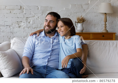Happy schoolkid son and dad sitting together on couch Happy schoolkid son and dad sitting together on couch 86579278