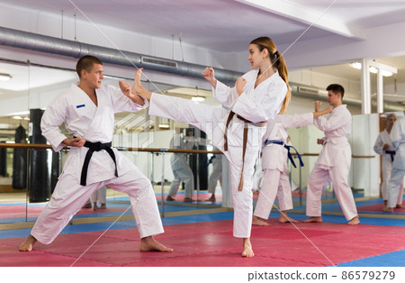 Woman and man in kimono and belts fighting during karate training Woman and man in kimono and belts fighting during karate training 86579279