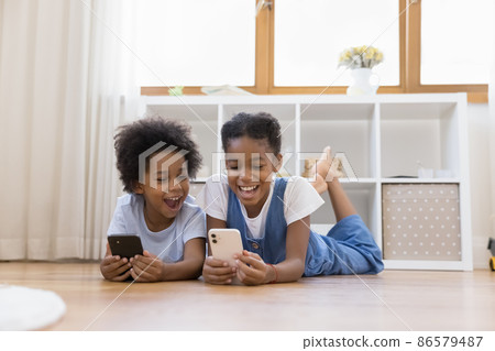 Little siblings lying on floor having fun using smartphones 86579487