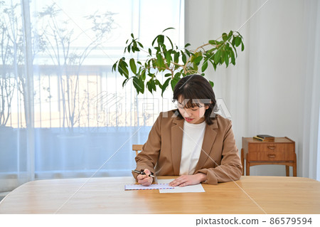 A woman writing an address on an airmail envelope at her desk 86579594