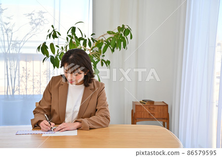 A woman writing an address on an airmail envelope at her desk 86579595