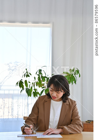 A woman writing an address on an airmail envelope at her desk 86579596