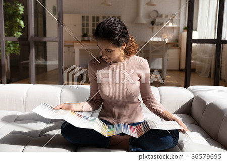 Woman sit on sofa looks at paint swatches palette Woman sit on sofa looks at paint swatches palette 86579695