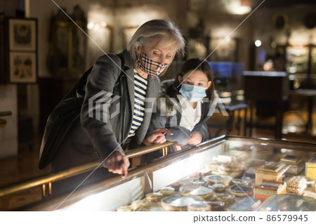 Preteen girl with grandmother in protective masks visiting historical museum Preteen girl with grandmother in protective masks visiting historical museum 86579945