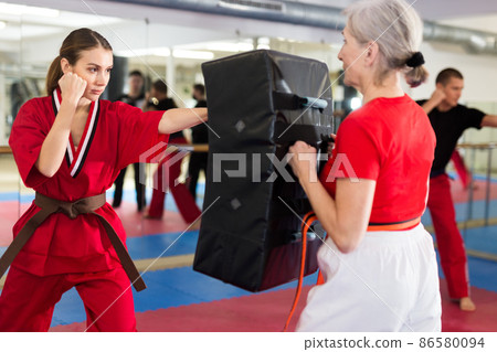 Young woman in red kimono launching blows on punch shield 86580094