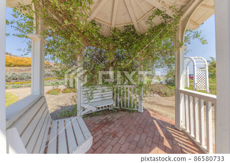 White gazebo with built-in seating and crawling plants 86580733