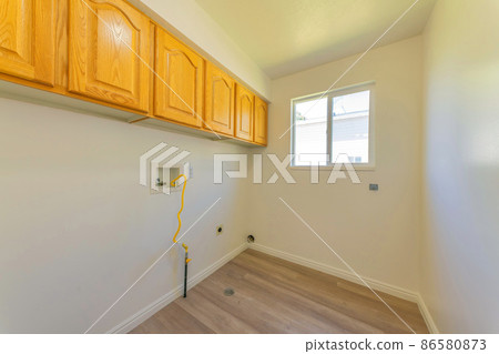 Empty laundry room with wooden wall cabinets and window 86580873