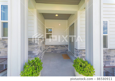 Entrance of a house with gray door on the side and two potted plants near the column posts Entrance of a house with gray door on the side and two potted plants near the column posts 86580911