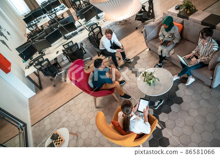 Top view photo of Multiethnic startup business team having brainstorming in relaxation area of modern office interior working on laptop and tablet computer 86581066