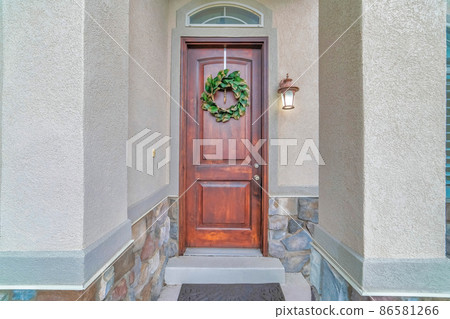 Wooden front door of a house with transom window and leafy wreath at the front 86581266