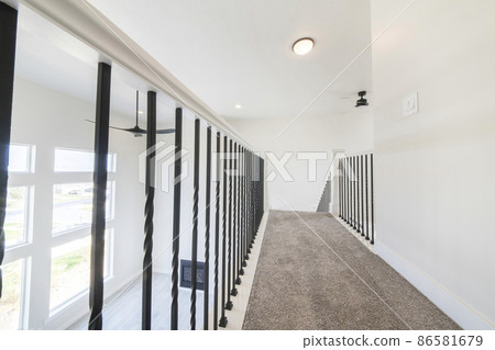Carpeted flooring on a hallway at the second floor of a house with white siding Carpeted flooring on a hallway at the second floor of a house with white siding 86581679