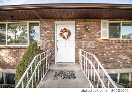 White front door of a house with wreath and colorful doormat White front door of a house with wreath and colorful doormat 86581691