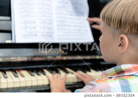 Caucasian boy 5 years old, preschooler, looks at the notes and plays the piano, view from the back. learning music. 86582384