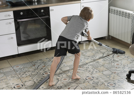 6-year-old boy is cleaning house, vacuuming kitchen floor 86582536