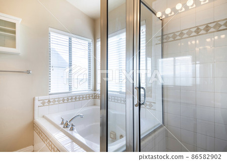 Bathroom interior with bathtub and shower stall with ceramic tiles surround near the windows Bathroom interior with bathtub and shower stall with ceramic tiles surround near the windows 86582902