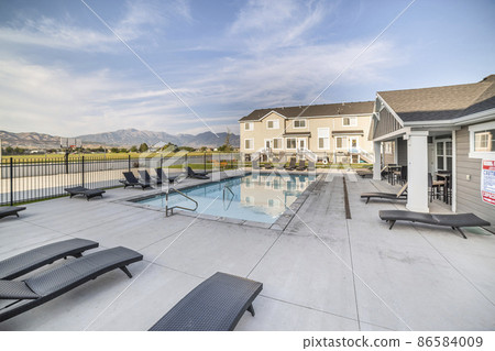 Community pool of a residential area with black lounge chairs and clubhouse 86584009